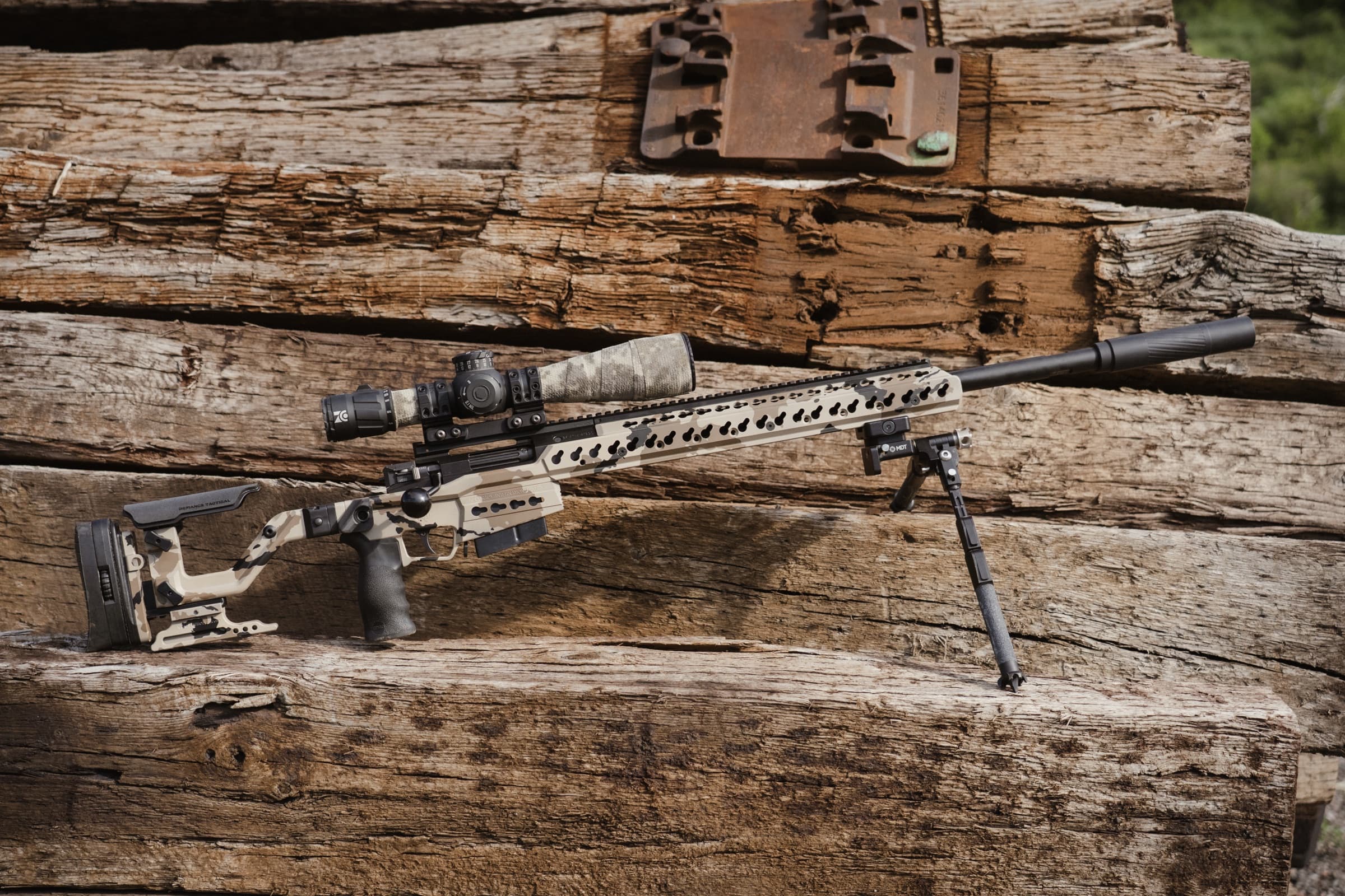 Precision rifle at rest on weathered timber, in soft daylight.